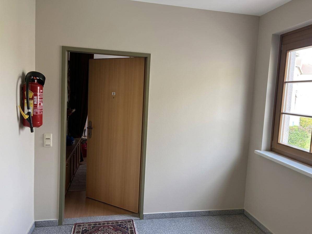 Heller Flur mit Holztür, Fenster und Fliesenboden im Eingangsbereich der Wohnung.