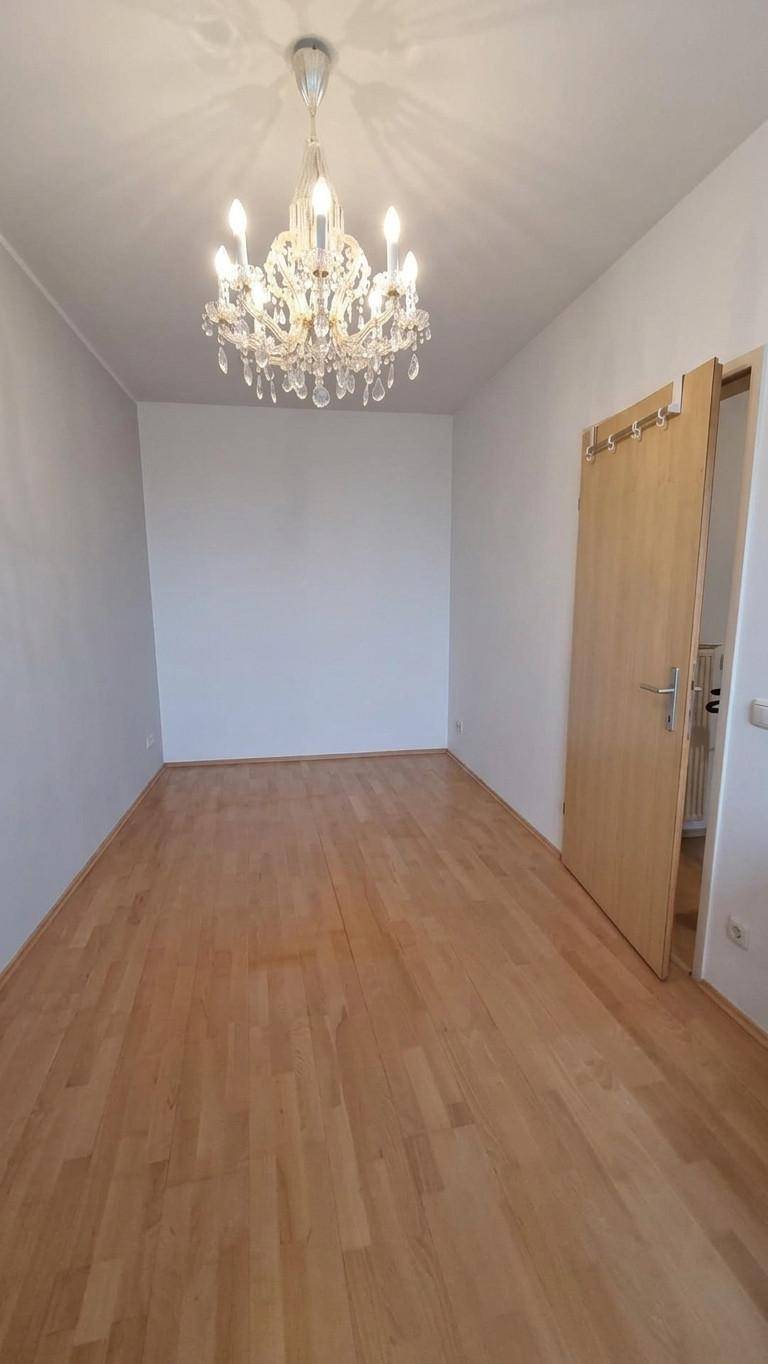 Leeres Zimmer mit Parkettboden, Kronleuchter und einer Holztür.