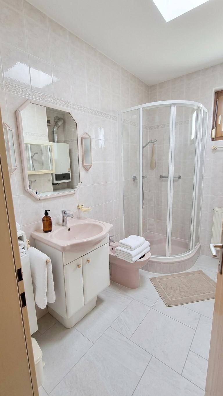 Helles Badezimmer mit Fliesen, Duschkabine, Waschbecken und Dachfenster.