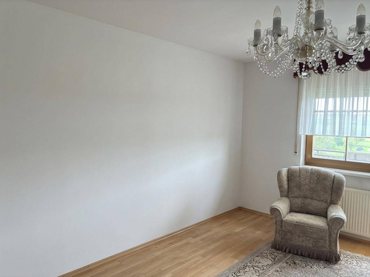 Gemütliches Wohnzimmer mit Parkettboden, Sessel und Fenster mit Vorhängen.