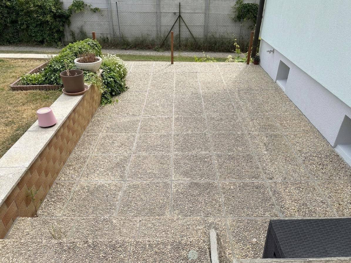 Gepflasterte Terrasse am Haus mit Blumenbeeten und Zugang zum Garten.
