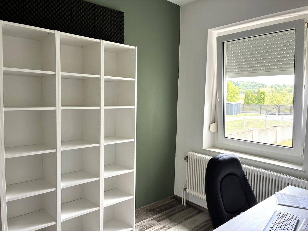 Arbeitszimmer mit weißem Regal, grün gestrichener Wand und Blick ins Grüne.
