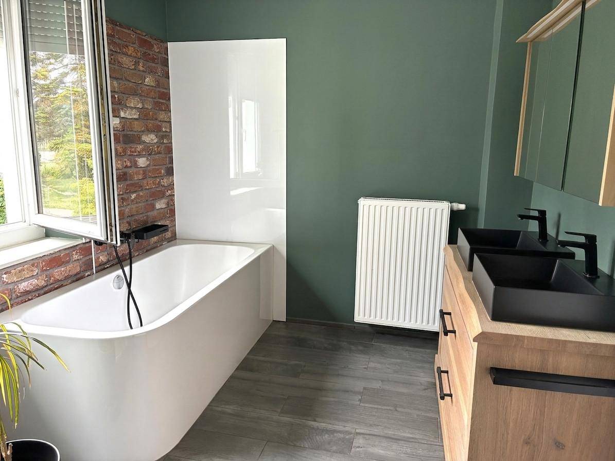 Modernes Badezimmer mit Badewanne, Doppelwaschbecken und grünen Wänden.