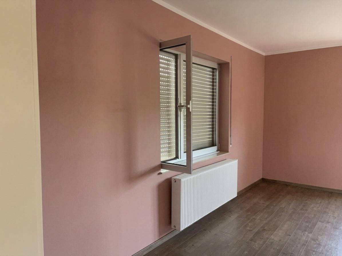 Leeres Zimmer mit rosafarbenen Wänden, Fenster mit Rollladen und Heizkörper.