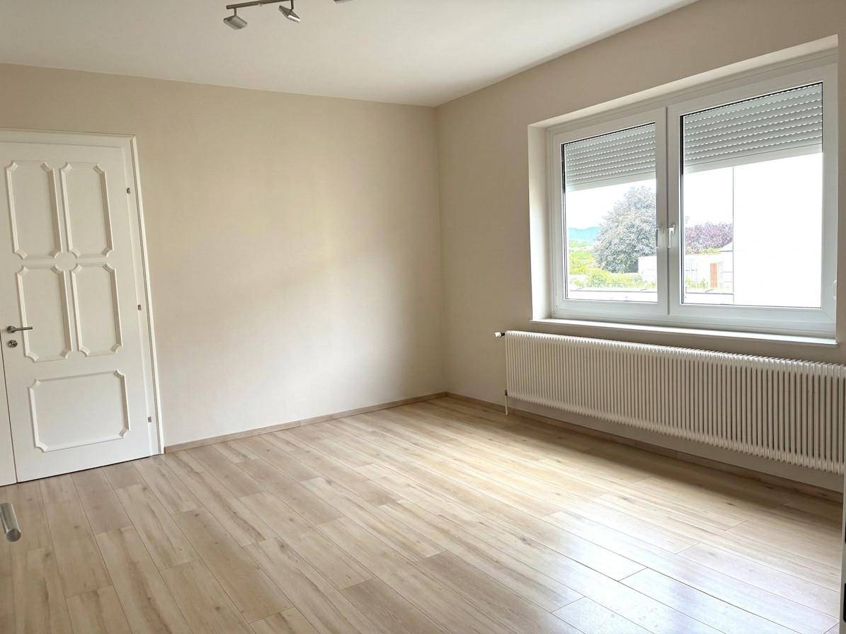 Helles Zimmer mit beigefarbenen Wänden, Laminatboden und großem Fenster.