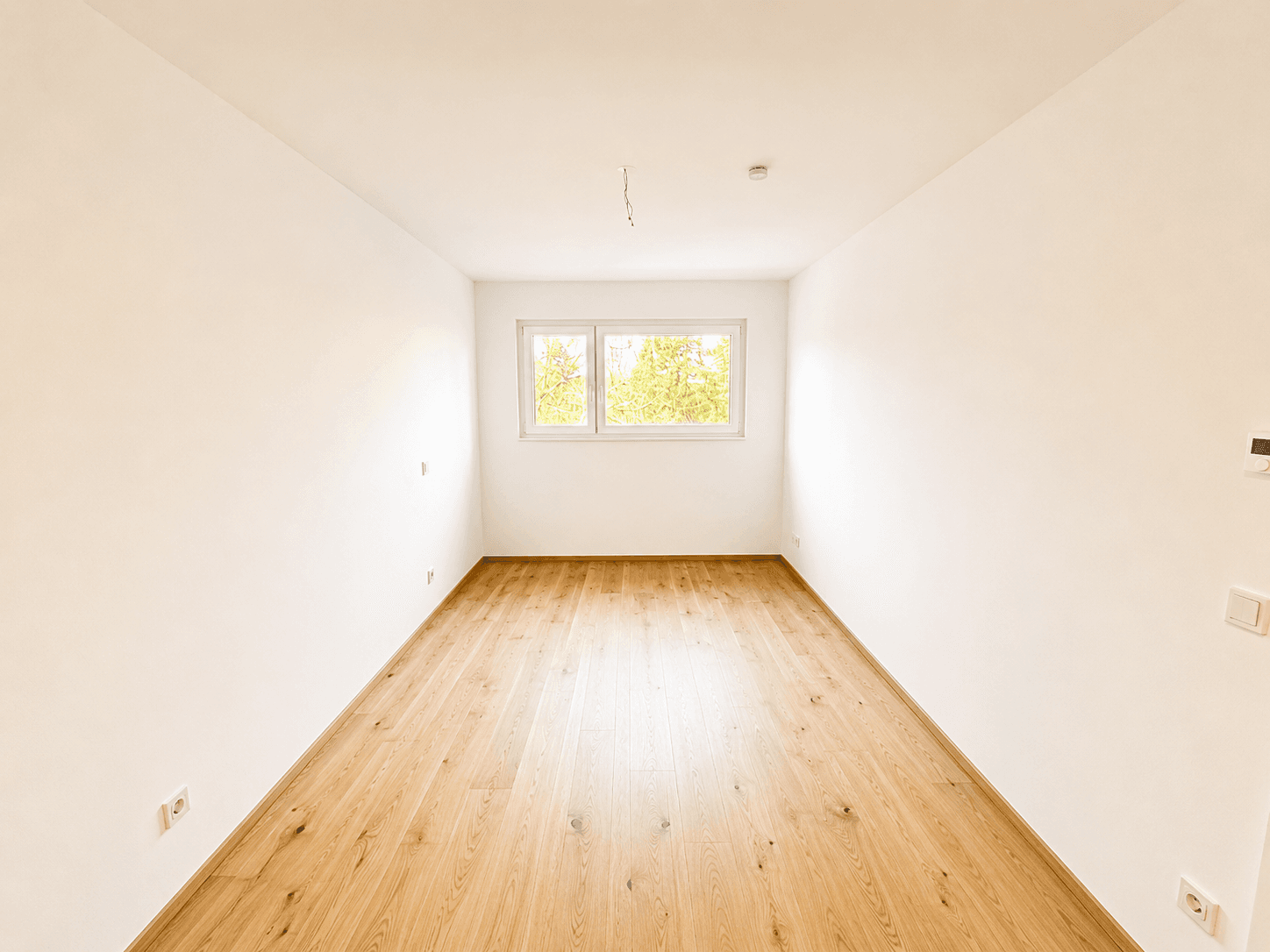 Kleiner, heller Raum mit Parkettboden und Fenster, ideal als Schlaf- oder Arbeitszimmer.