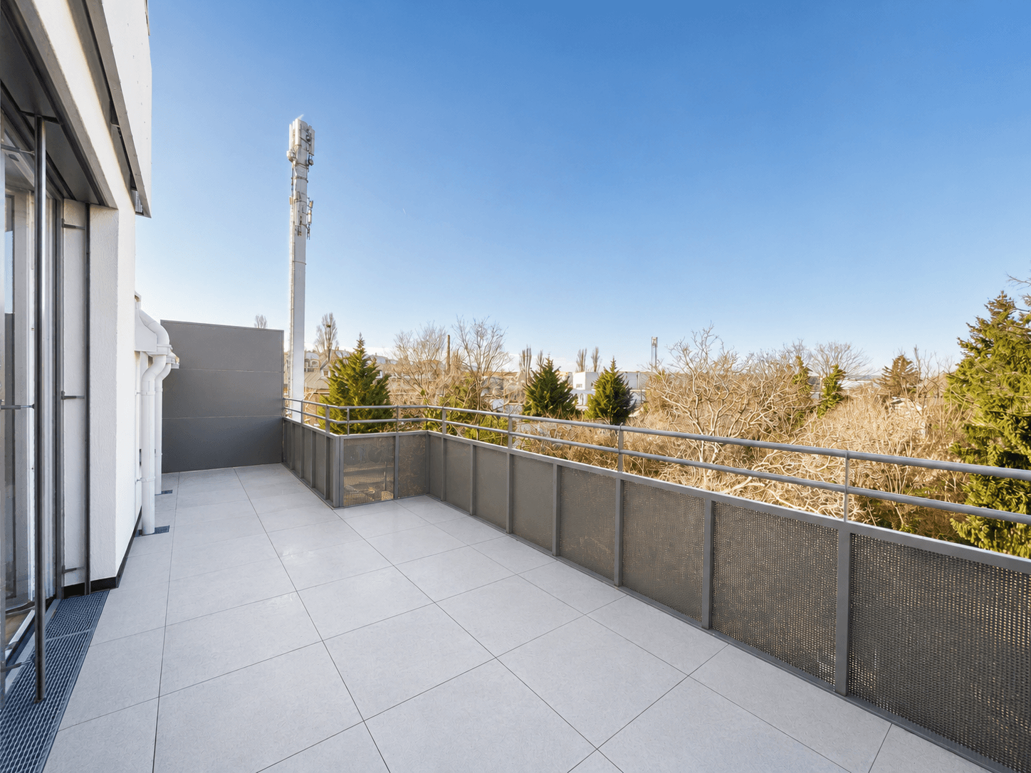 Große, geflieste Terrasse mit modernem Metallgeländer und weitem Blick über die Umgebung und Bäume.