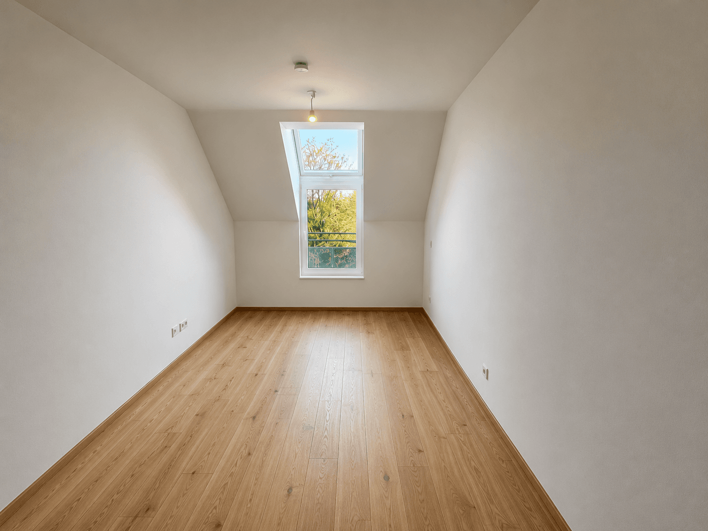 Helles Schlafzimmer im Dachgeschoss mit schrägen Wänden, Laminatboden und einem großen Dachfenster.