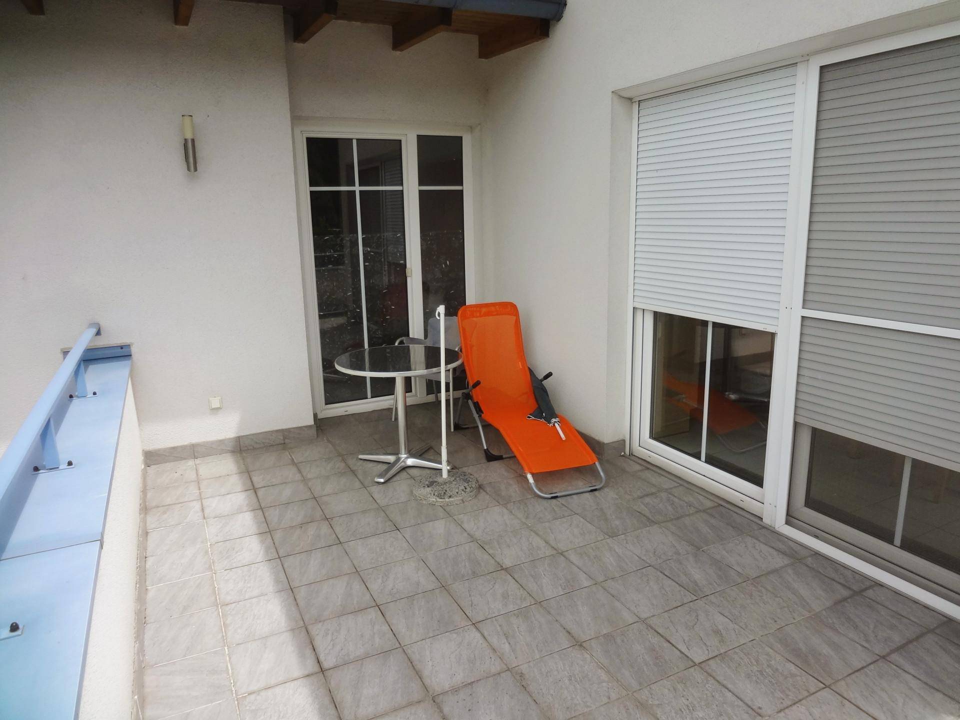 Kleiner gefliester Balkon mit Tisch und Stuhl, geschützt durch Rollläden.
