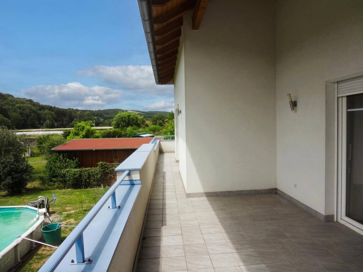 Langer Balkon mit blauer Brüstung und Blick auf den Garten und die Umgebung.