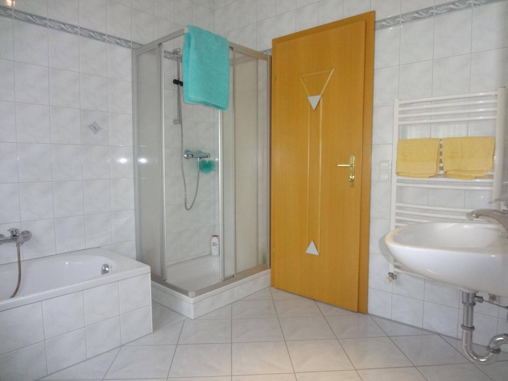 Badezimmer mit Badewanne, Dusche, Waschbecken und hellen Fliesen.