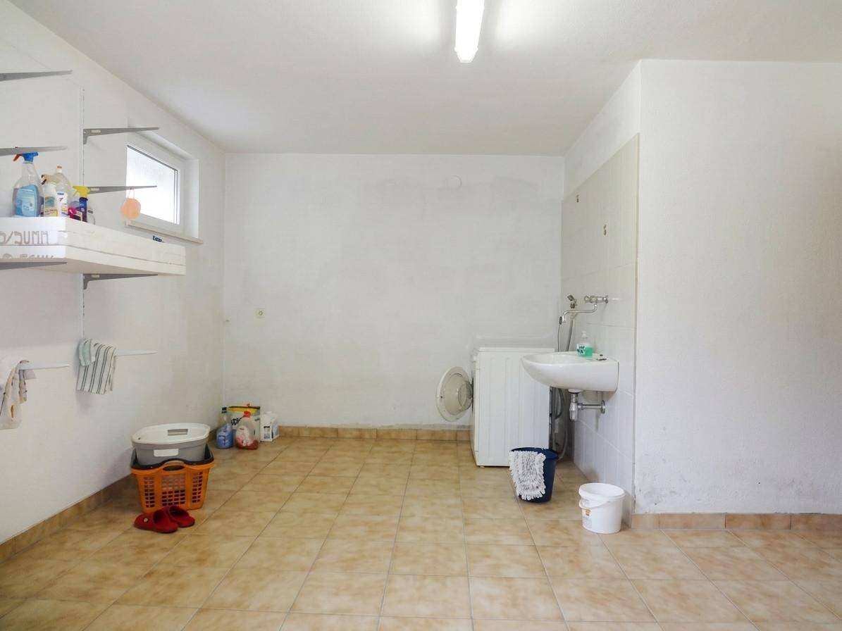 Hauswirtschaftsraum mit Waschmaschine, Waschbecken und Regalen für Vorräte.