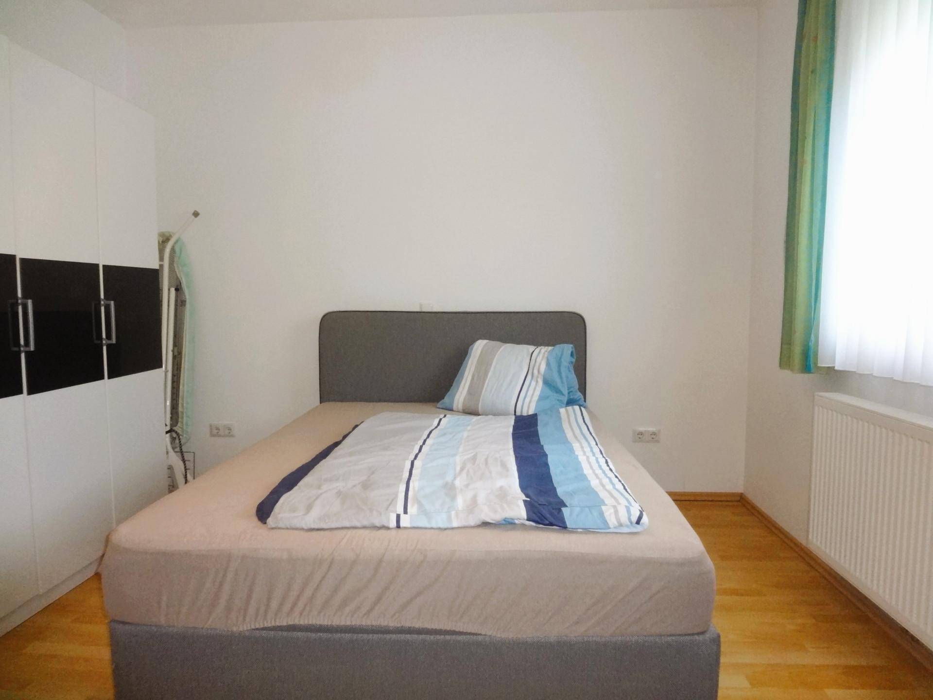 Schlafzimmer mit Doppelbett, weißem Kleiderschrank und Laminatboden.