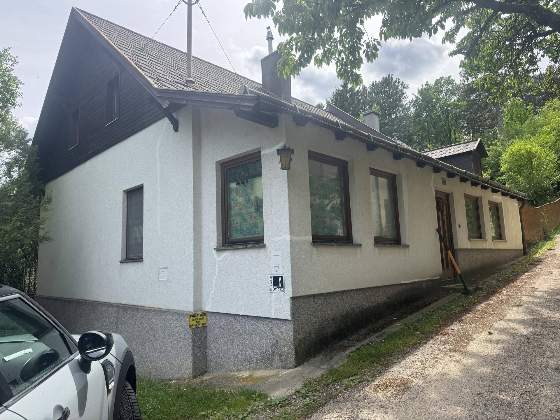 Seitenansicht eines weiß verputzten Hauses mit braunen Fenstern und einem klassischen Satteldach.