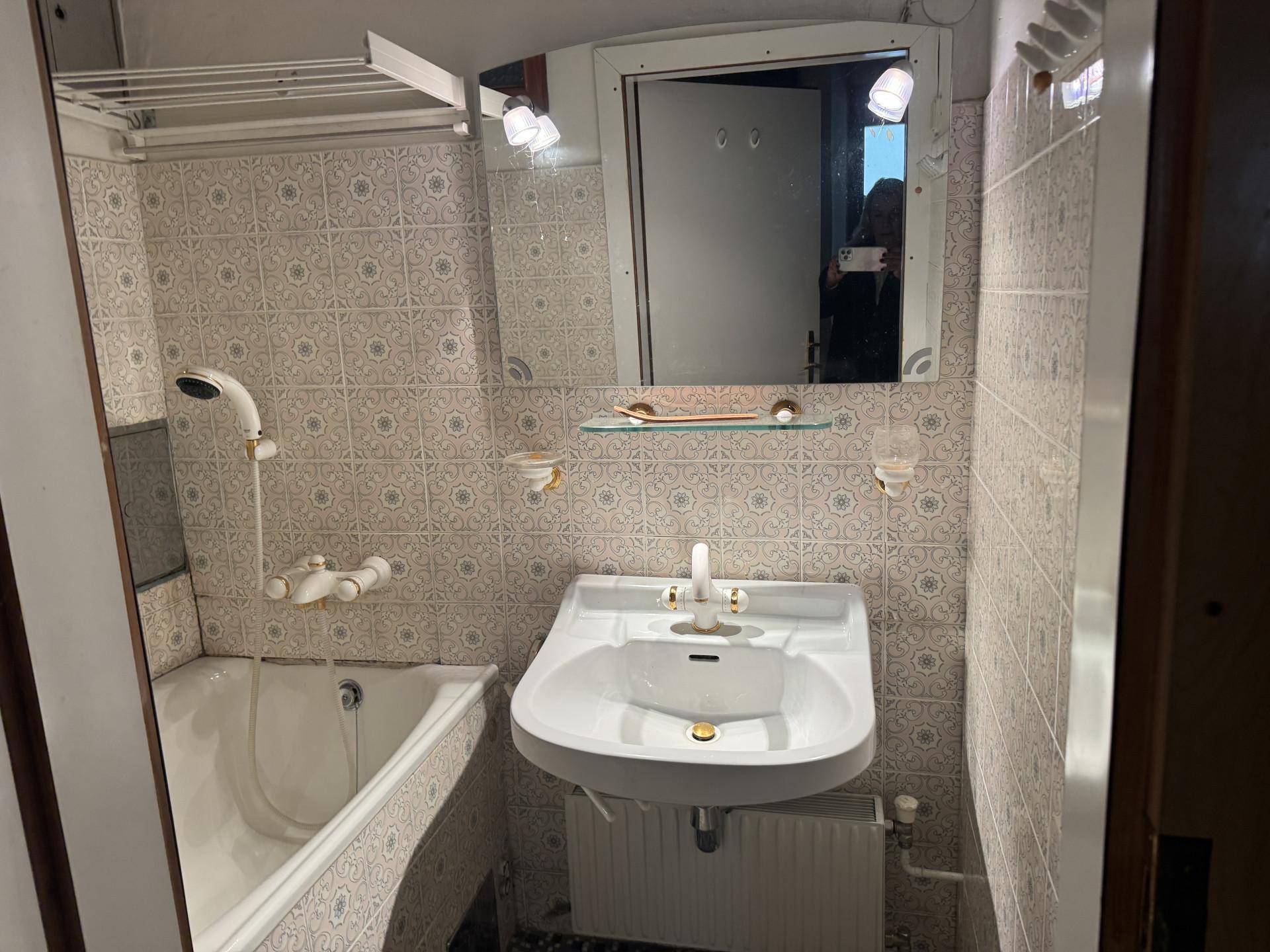Kleines Badezimmer mit Badewanne, Waschbecken und gemusterten Fliesen im Stil der 80er Jahre.