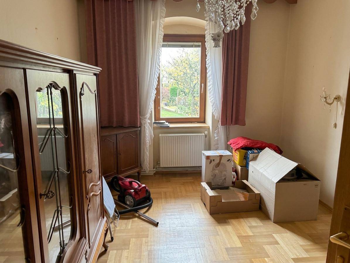 Schlafzimmer mit Parkettboden, großem Fenster und einem eleganten Kronleuchter an der Decke.