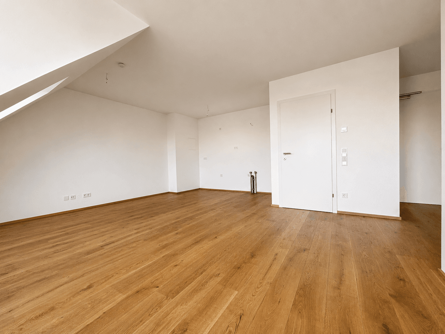 Geräumiger Dachgeschossraum mit Holzboden, Schrägdecke und weißer Tür in neuwertigem Zustand.
