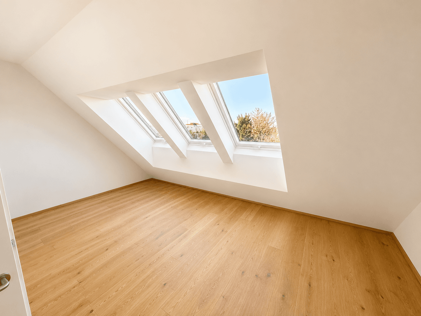 Helles Dachzimmer mit Holzboden, schrägen Wänden und mehreren Dachfenstern für viel Tageslicht.