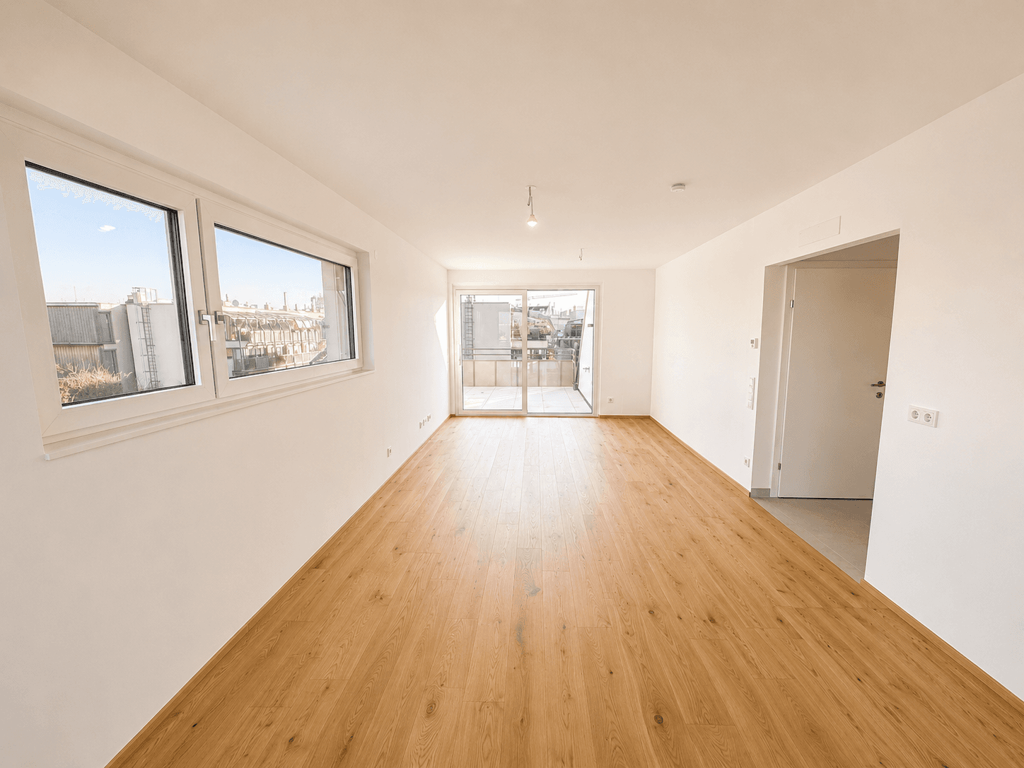 Geräumiges, helles Zimmer mit Holzboden, großen Fenstern und Zugang zu einem Außenbereich.