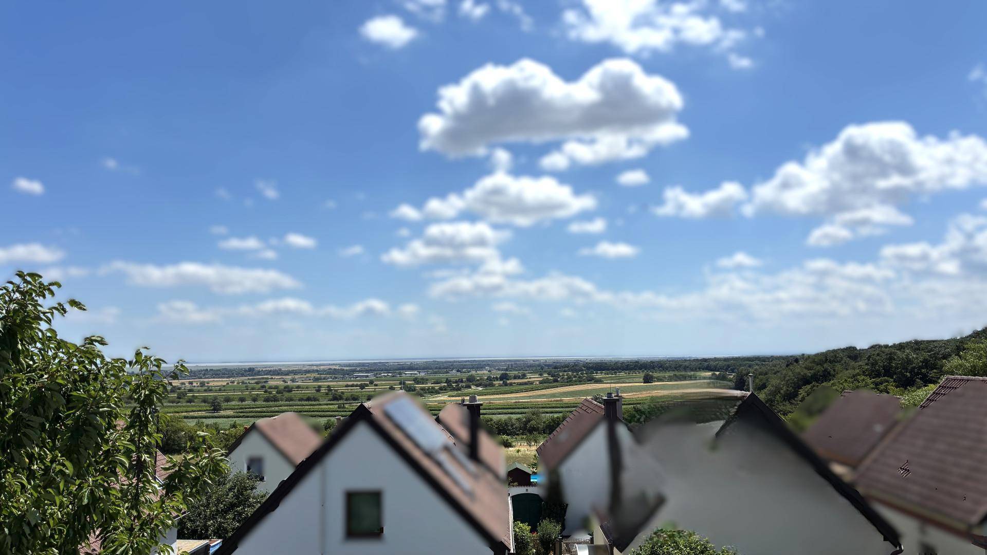 Panoramablick über eine weite, flache Landschaft mit Feldern und Häusern unter bewölktem Himmel.