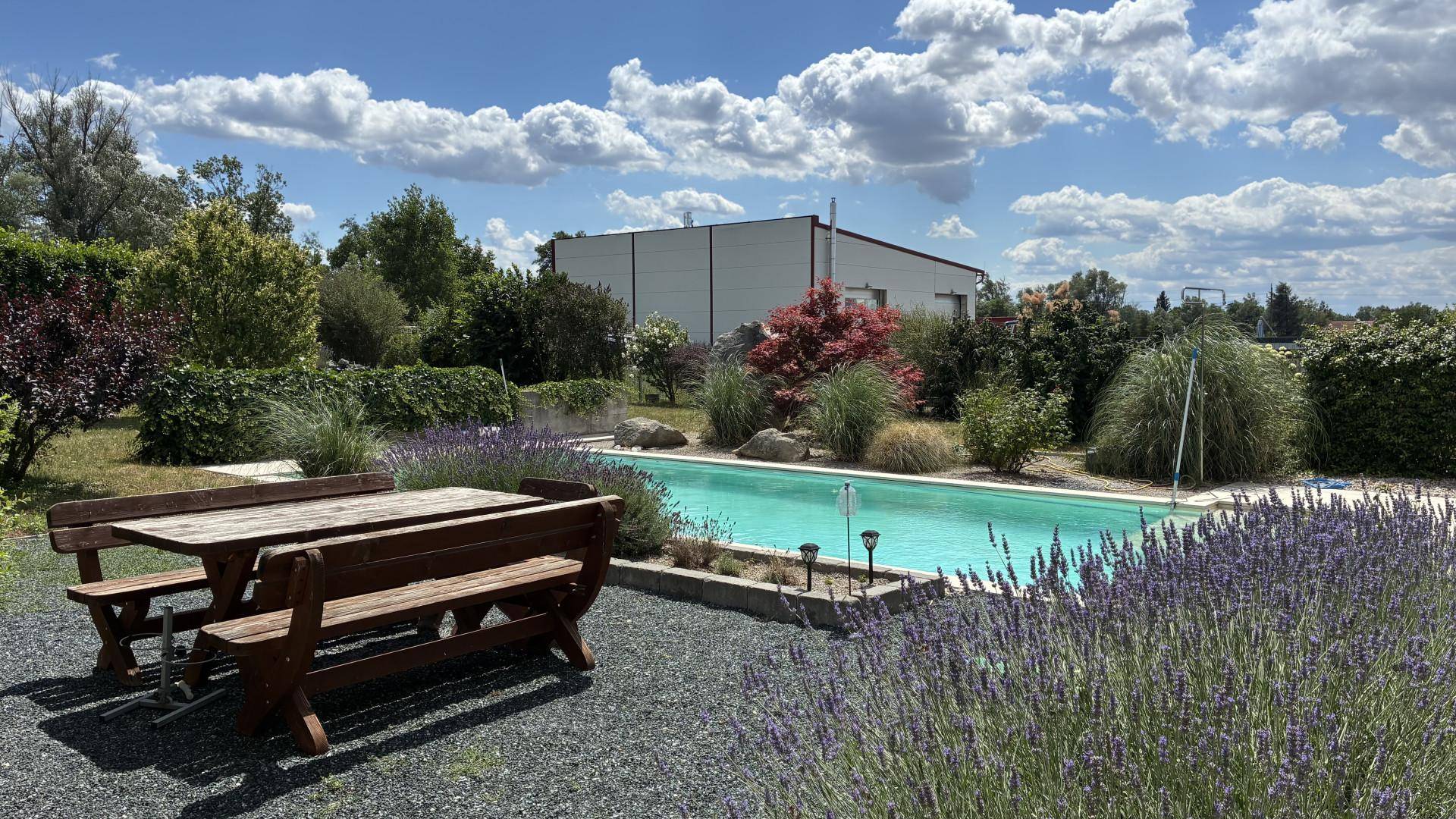 Weitläufiger Garten mit Swimmingpool, rustikalem Holztisch und blühendem Lavendel.