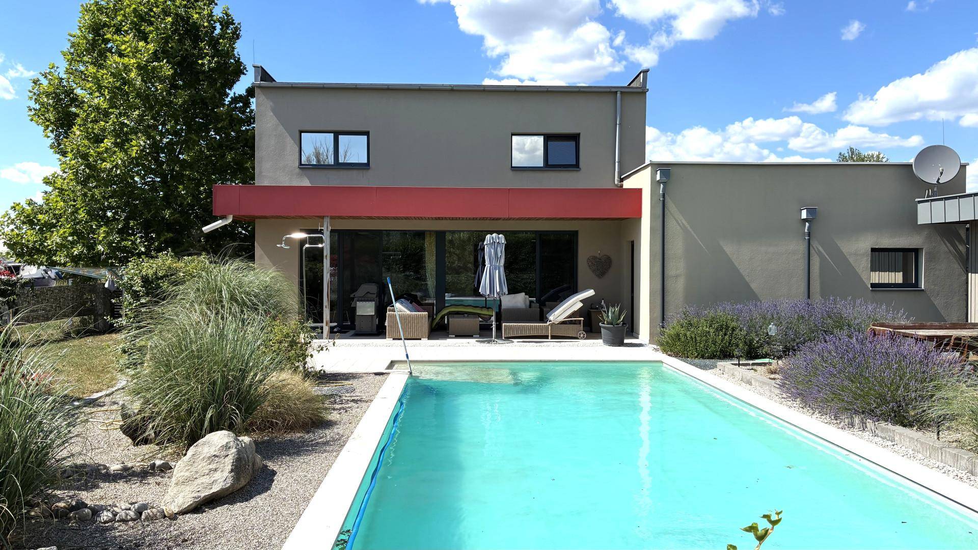 Modernes Haus mit großem Swimmingpool, Sonnenterrasse und Garten unter blauem Himmel.