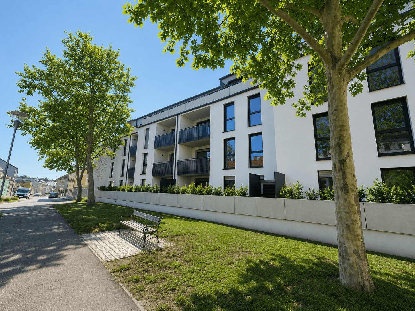 Moderne Wohnanlage mit weißer Fassade, schwarzen Fenstern und Balkonen, umgeben von gepflegten Grünflächen und Bäumen.
