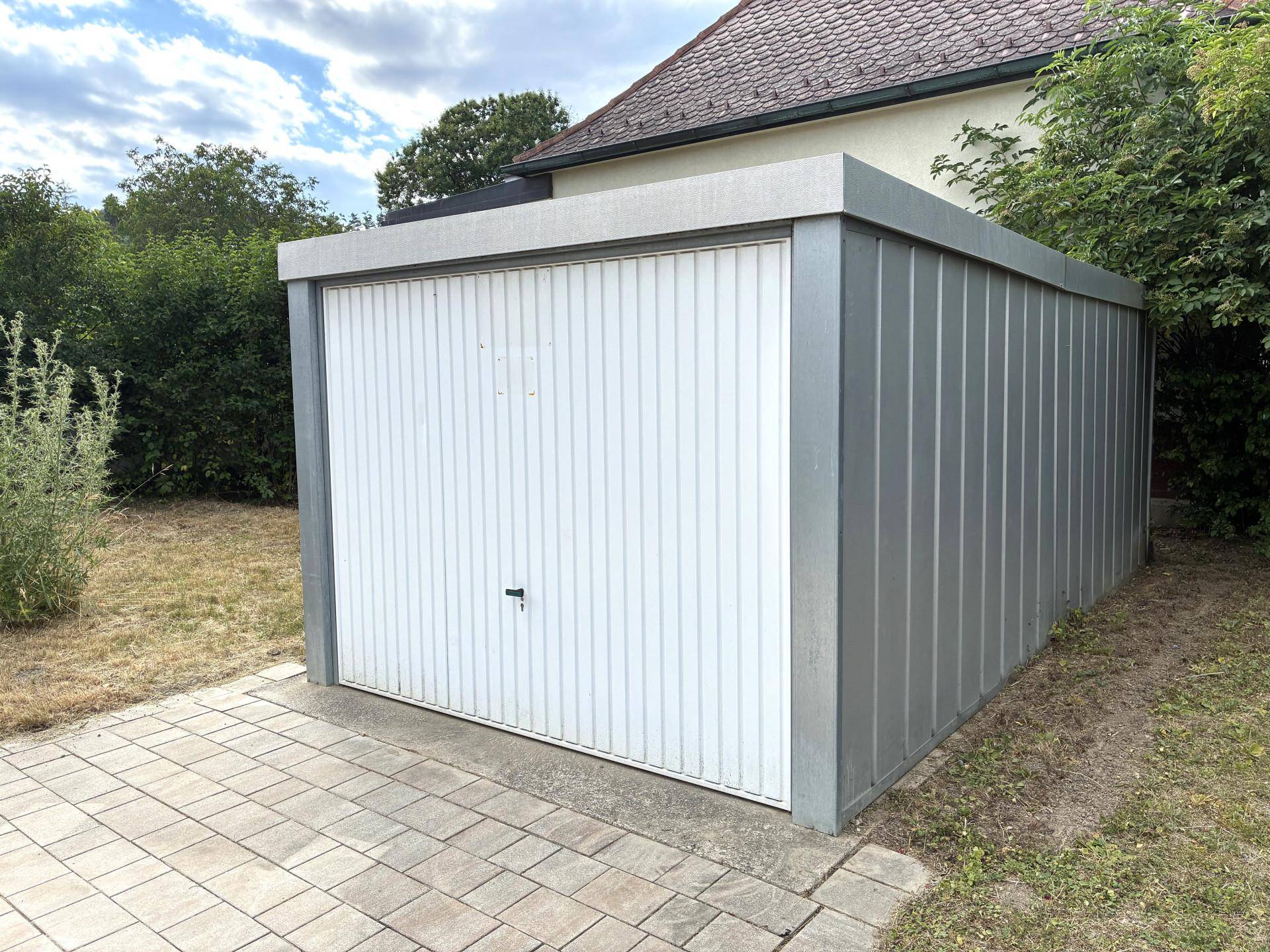 Freistehende Garage mit weißem Rolltor und grauen Seitenwänden.