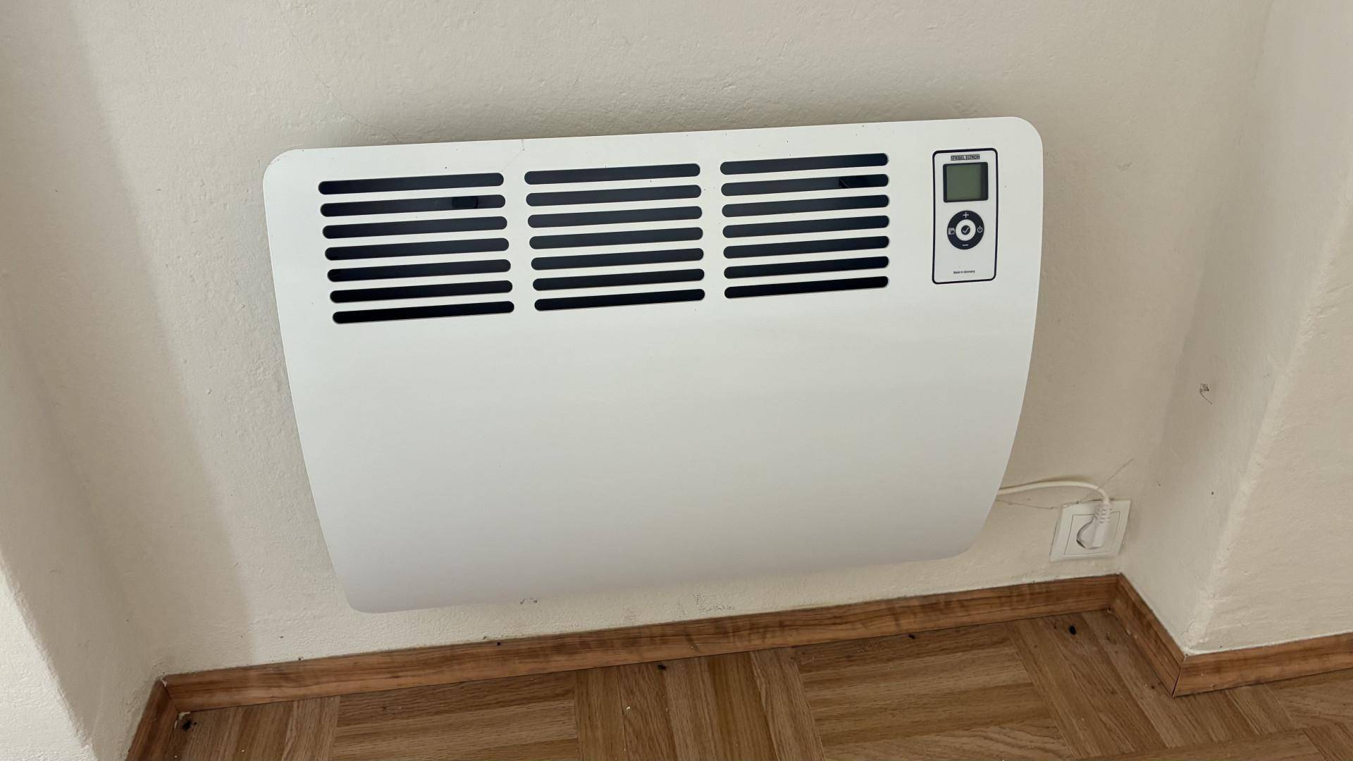 Wandmontierter Elektroheizer mit digitaler Anzeige über Parkettboden.