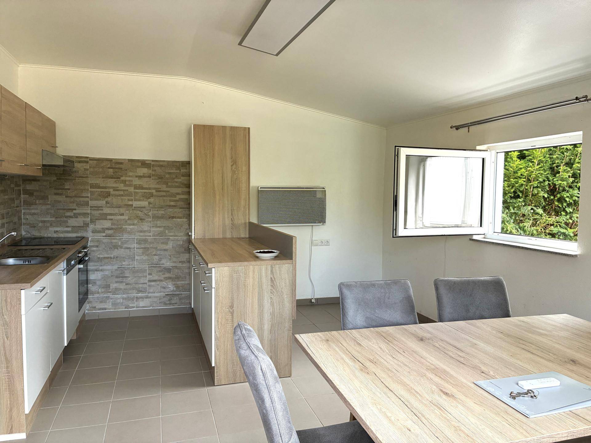 Moderne Küche mit Holzelementen, Essbereich und Blick ins Grüne durch das Fenster.