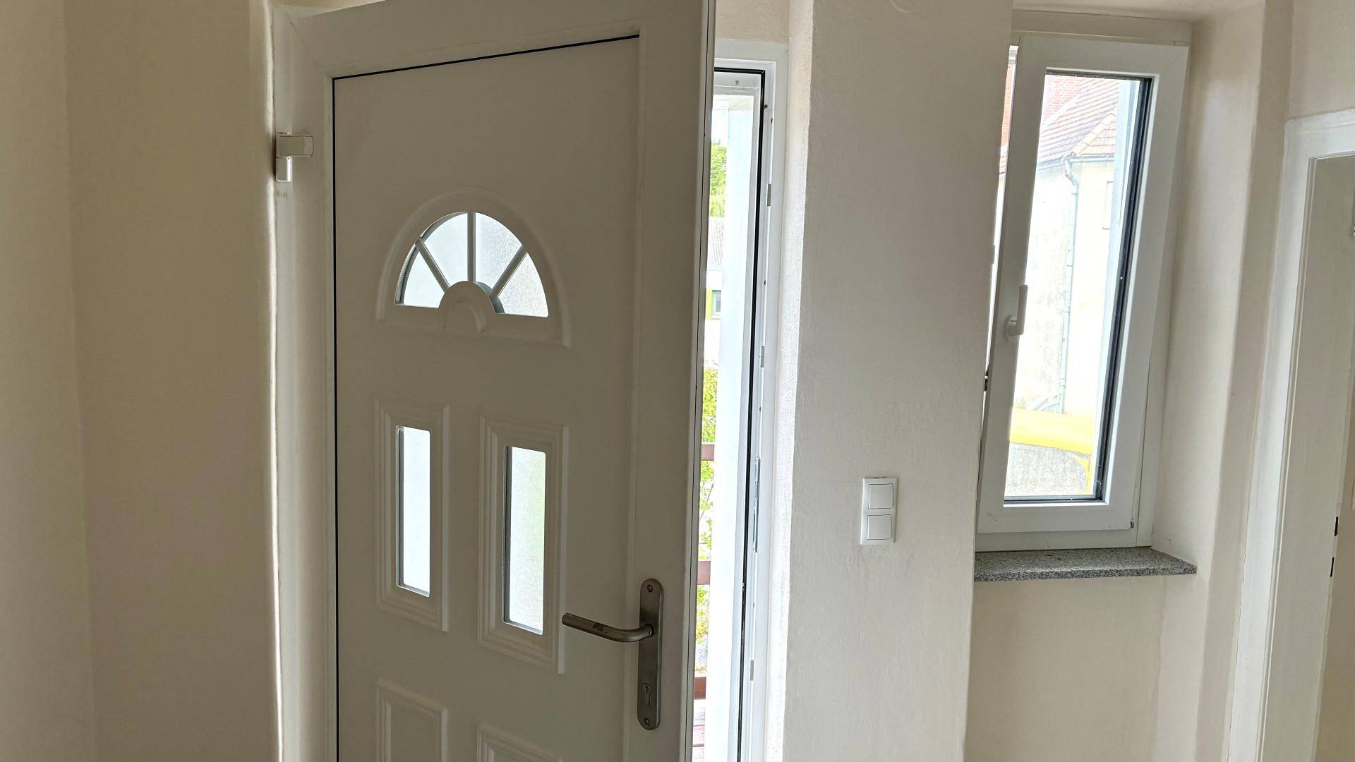 Heller Eingangsbereich mit weißer Tür und Fenster, das Tageslicht hereinlässt.