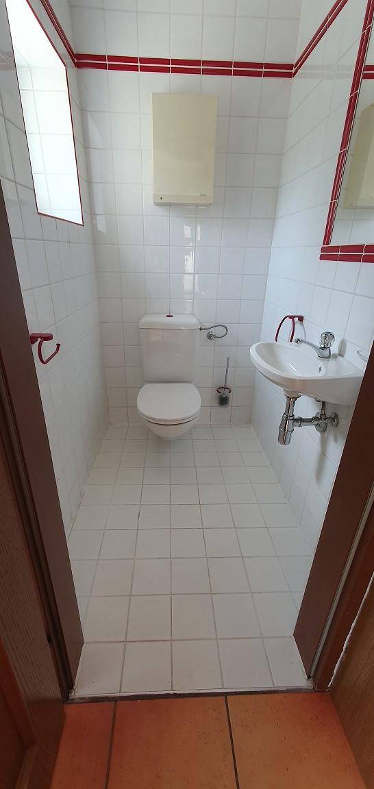 Separates WC mit Toilette, Waschbecken und weißen Fliesen.