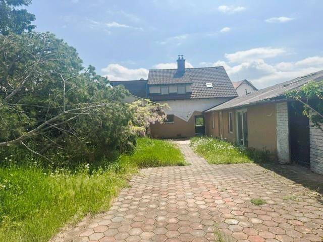 Rückansicht des Hauses mit gepflastertem Hof und Nebengebäude unter blauem Himmel und Bäumen.