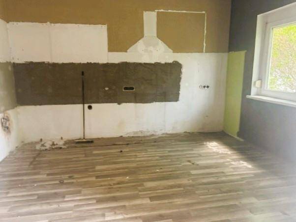 Leerer Küchenraum im Rohbau mit vorbereiteten Anschlüssen und neuem Laminatboden.