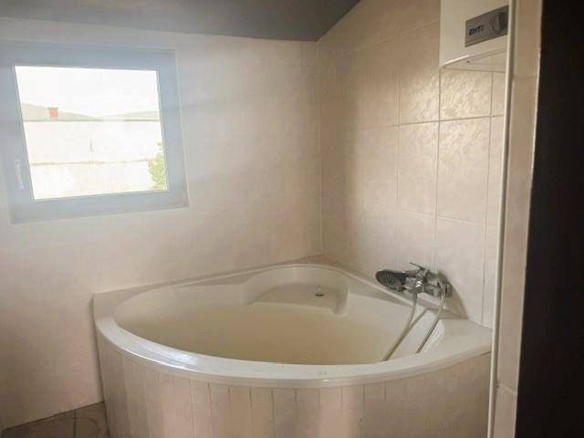 Badezimmer mit beigefarbenen Fliesen und einer Eckbadewanne unter einem Fenster.