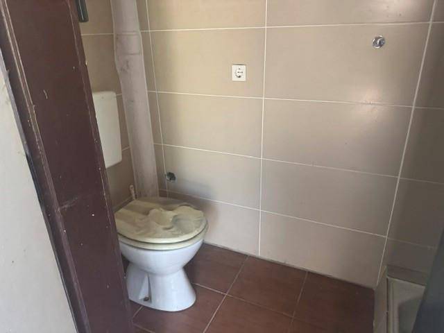 Kleines WC mit beigefarbenen Fliesen und einfacher Toilette, in renovierungsbedürftigem Zustand.