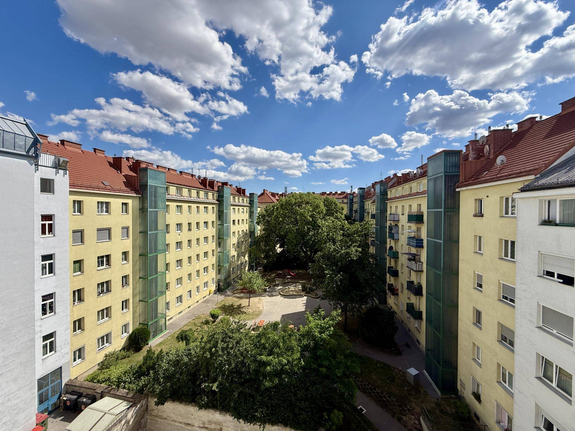 Innenhof mit Grünflächen, Bäumen und Spielplatz, umgeben von Wohngebäuden.
