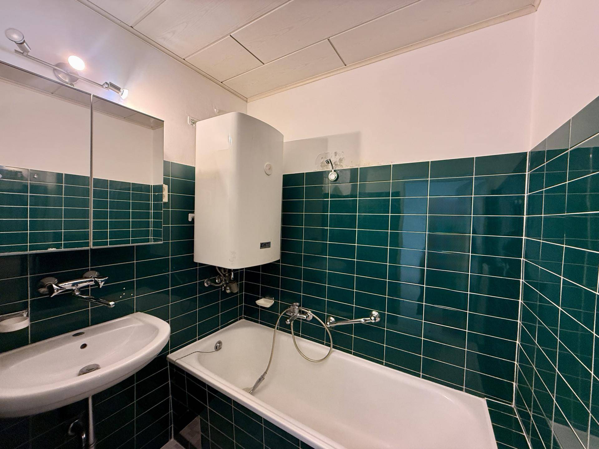 Badezimmer mit dunkelgrünen Wandfliesen, Badewanne, Waschbecken und Spiegelschrank.