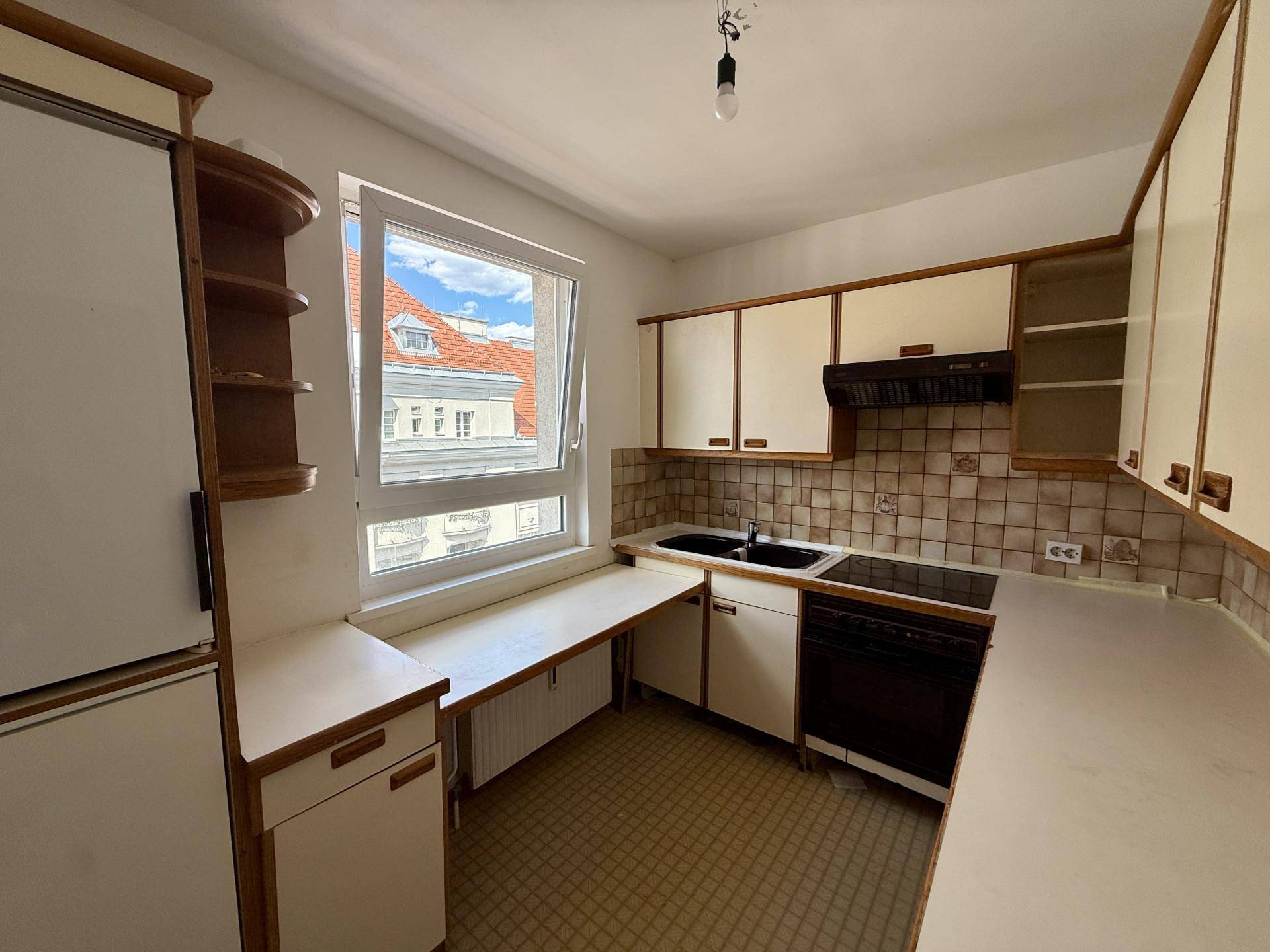 Funktionale Küche mit älteren Einbauschränken, Fliesenrückwand und Fensterblick.