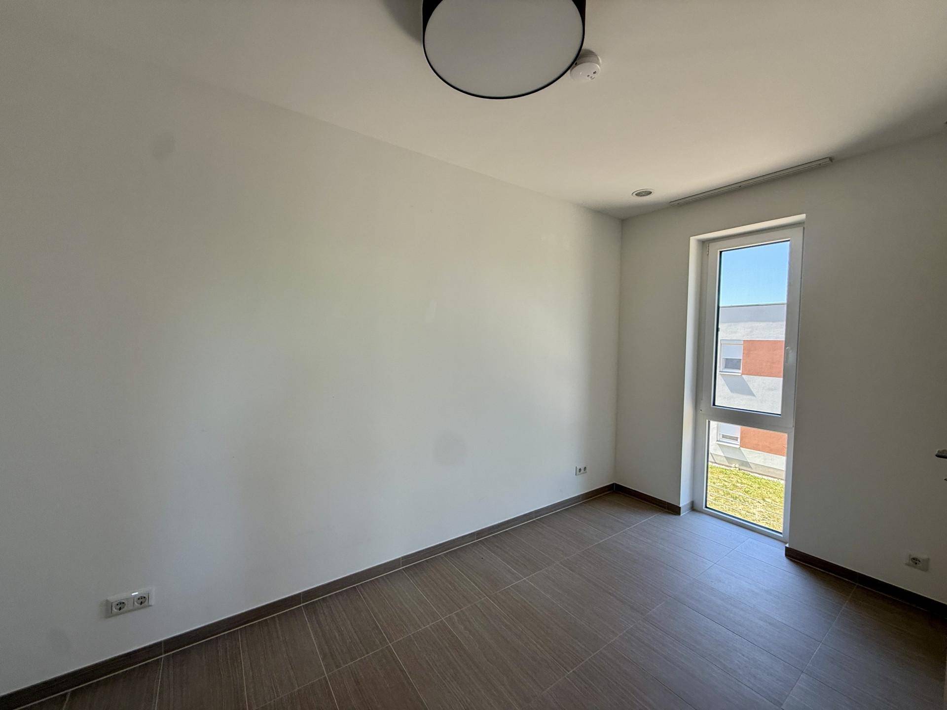 Helles Zimmer mit Fliesenboden und einem hohen Fenster, das viel Tageslicht hereinlässt.