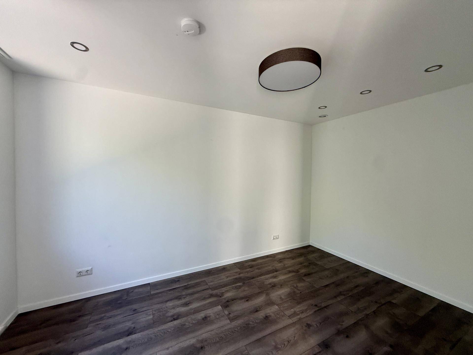 Geräumiges Zimmer mit dunklem Laminatboden und moderner Deckenbeleuchtung.