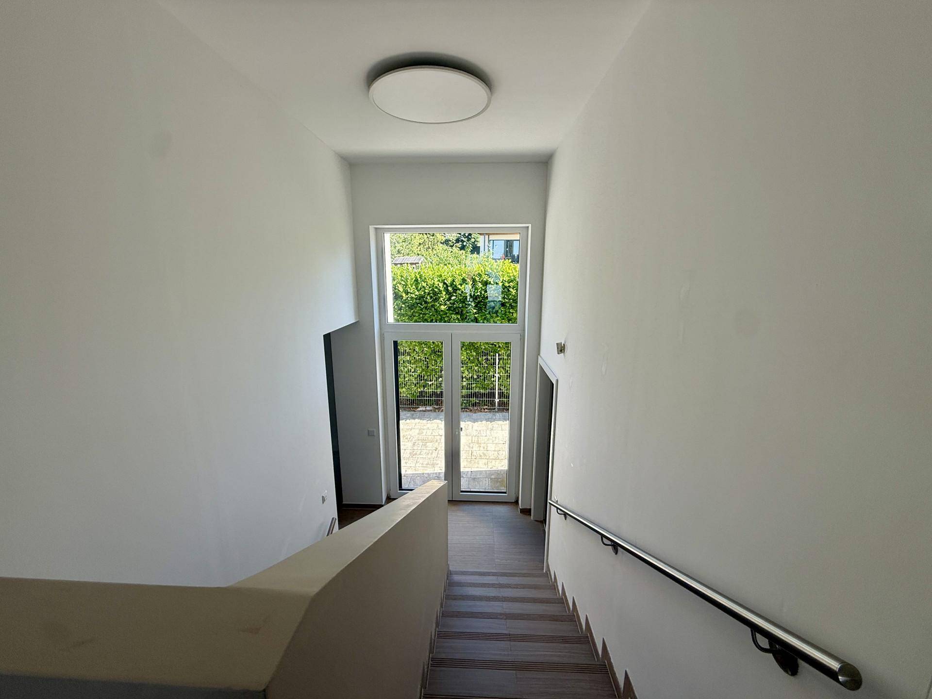 Heller Treppenaufgang mit Handlauf und großem Fenster, das den Eingangsbereich erhellt.