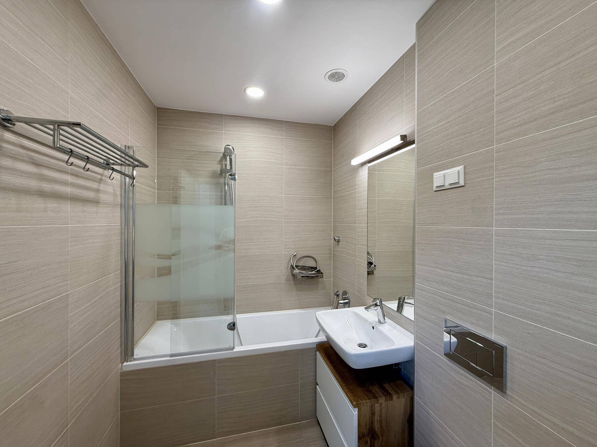 Modernes Badezimmer mit beigefarbenen Fliesen, Badewanne mit Duschabtrennung und Einzelwaschbecken.