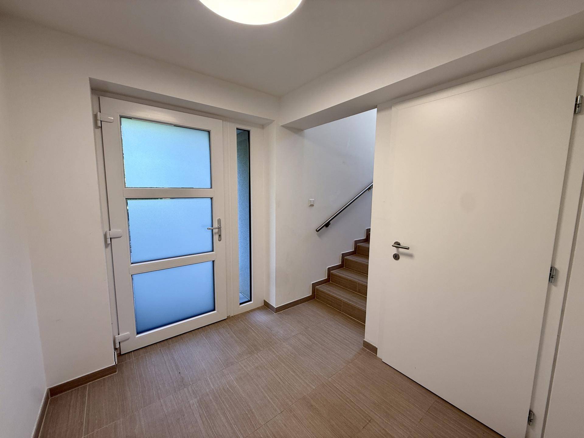 Eingangsbereich mit Fliesenboden, moderner Tür und Zugang zum Treppenhaus.