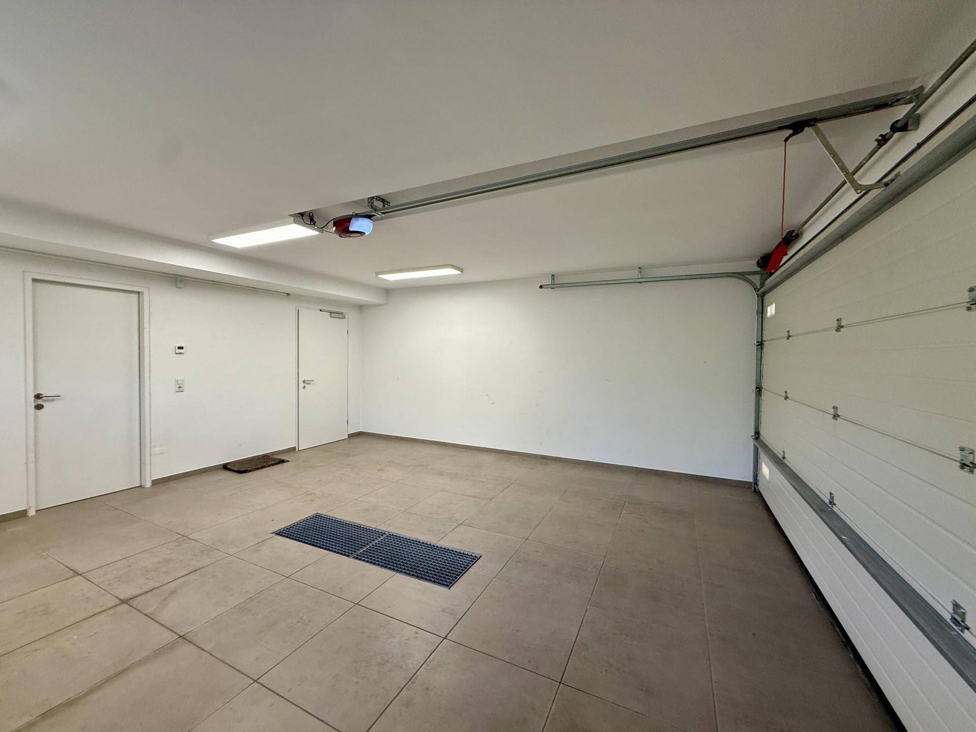 Geräumige Garage mit Fliesenboden, automatischem Tor und ausreichend Platz für Fahrzeuge.
