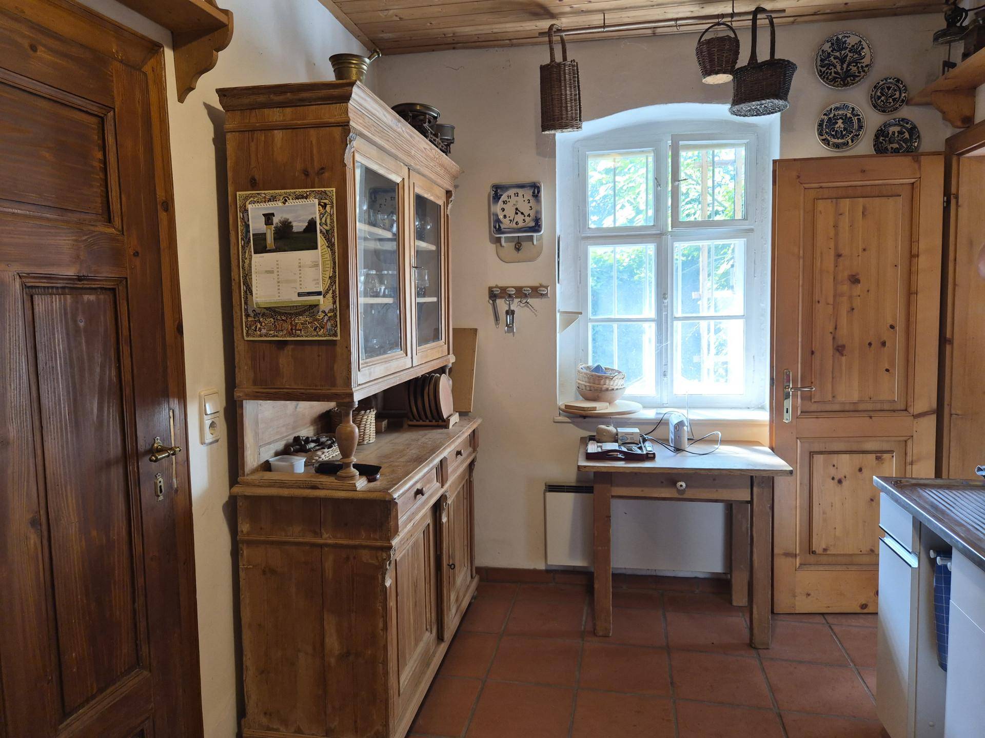 Rustikale Küche mit Holzschränken, Terrakottaboden und traditionellen Dekorationen am Fenster.