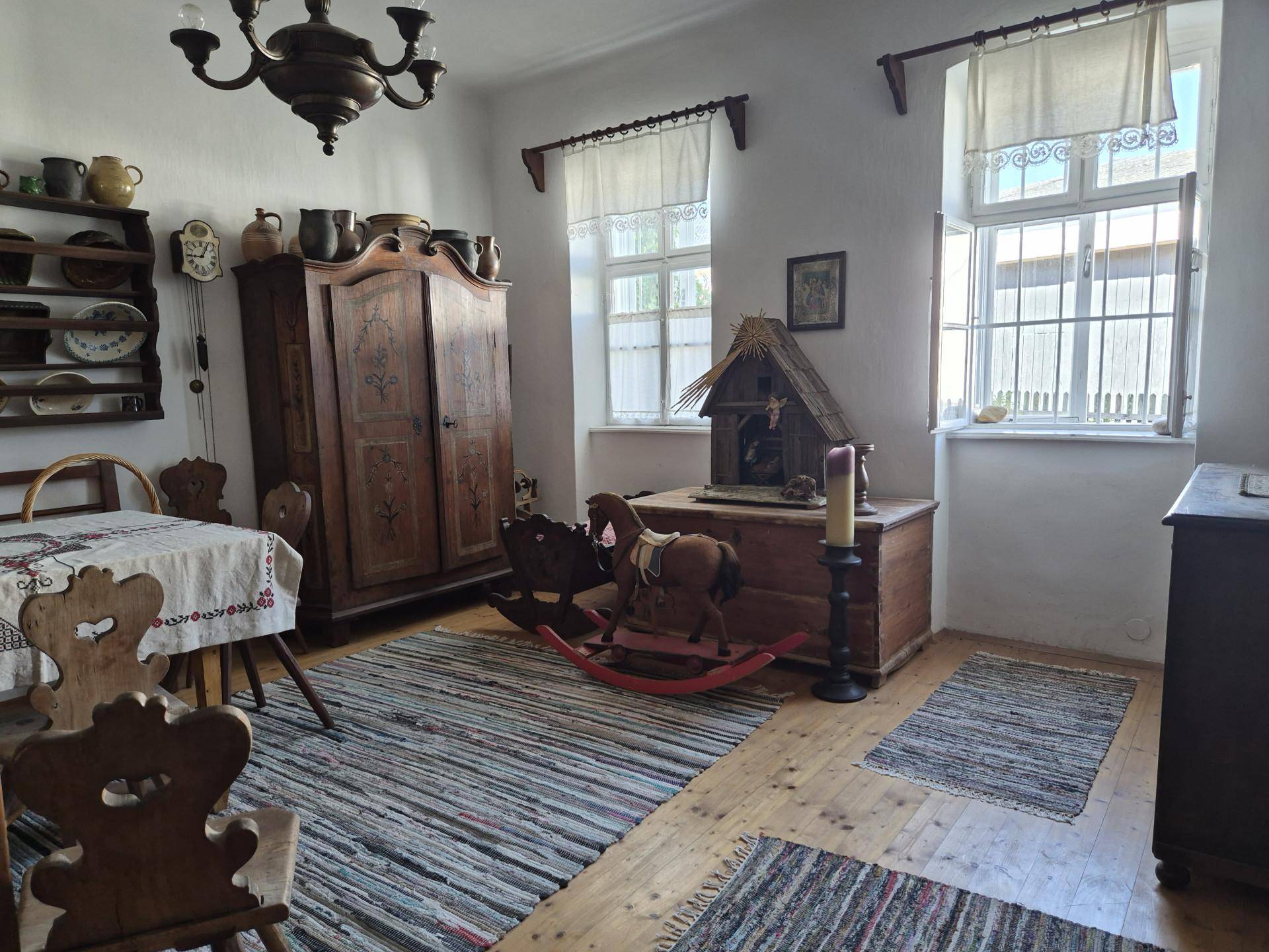 Wohnzimmer mit traditionellen Holzmöbeln, Teppichen und Fenstern mit Vorhängen.