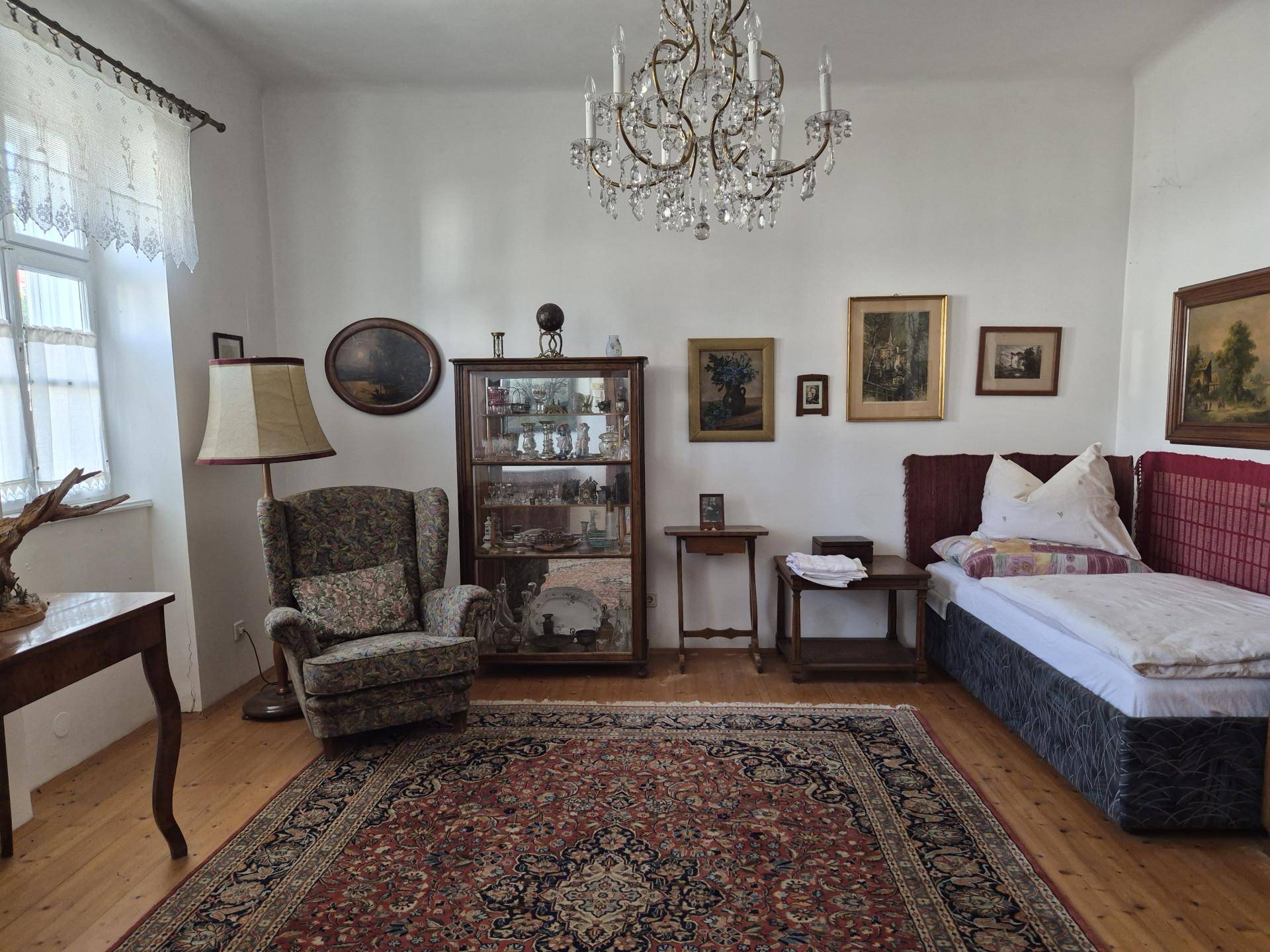 Schlafzimmer mit Einzelbett, antikem Sessel, Kronleuchter und traditionellem Teppich.