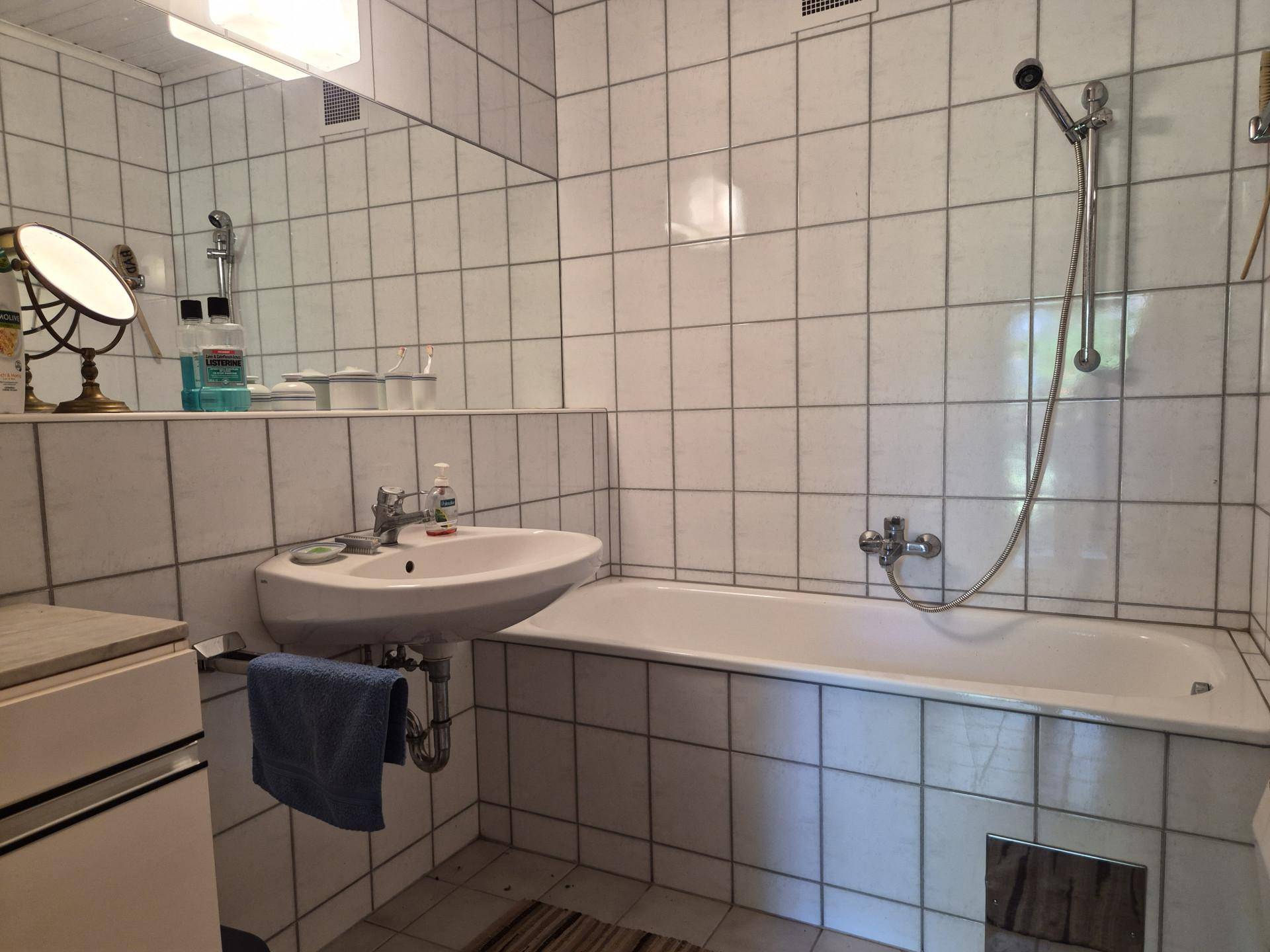 Badezimmer mit weißen Fliesen, Badewanne und Waschbecken, ausgestattet mit einem Spiegel.