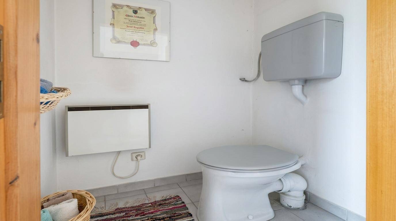 Separate Toilette mit Wandheizung und traditionellem Spülkasten.